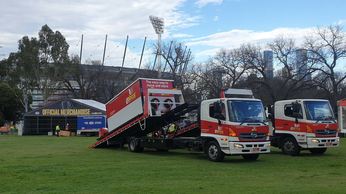Two gobox trucks unloading storage units beside the Official Merchandise marquee at the MCG